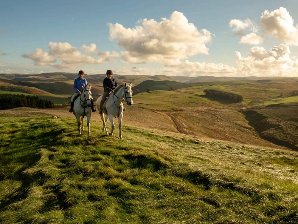 Couple riding on horses near Forter Castle in the Scotish Highlands